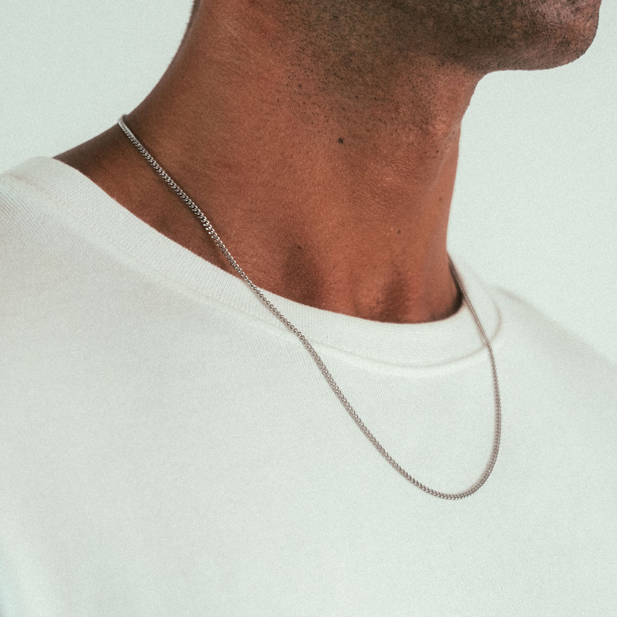 The close-up features a person wearing the WAV Cuban Chain Necklace, a sleek custom jewelry piece. Paired with a light knit top, the image shows just their neck and lower face against a neutral background, highlighting the elegant design.