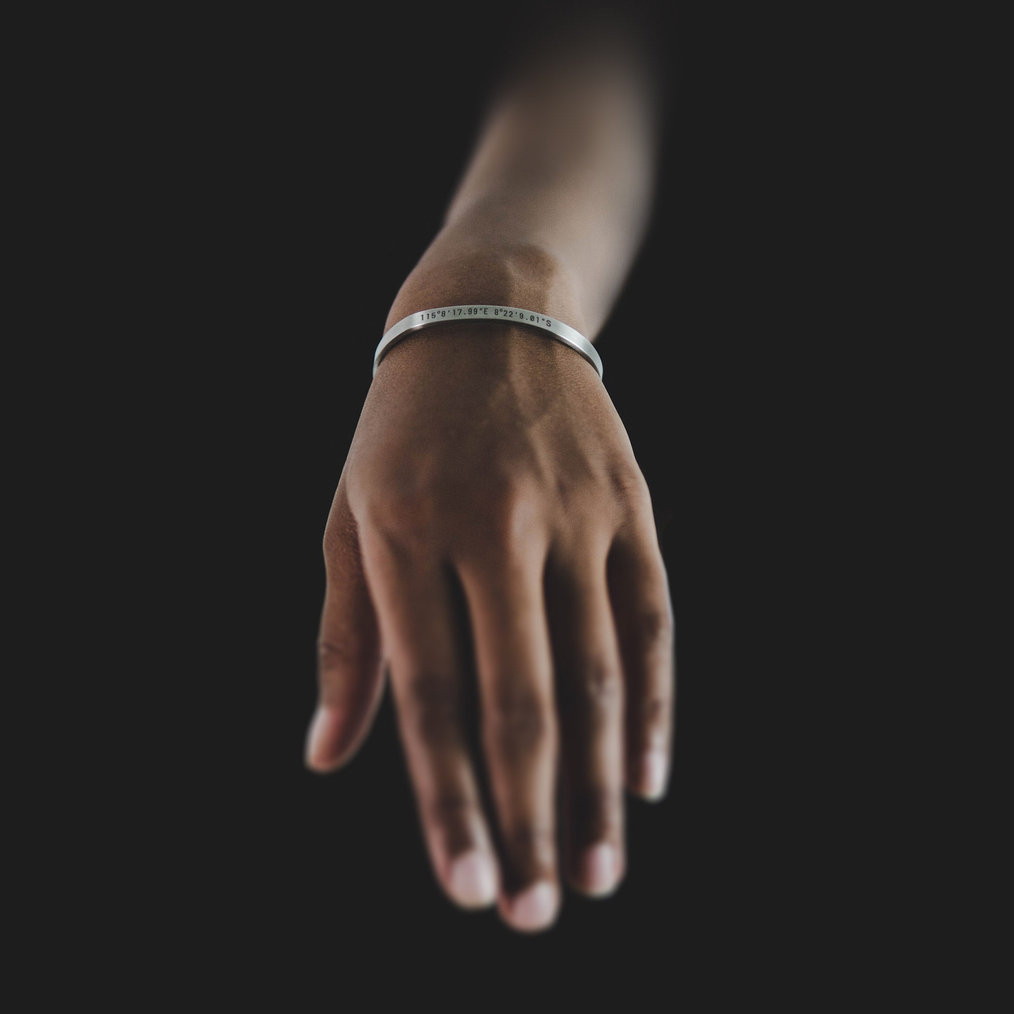 Custom cuff bracelet on a woman's wrist, made of stainless steel 316L with 18k gold PVD plating, customized and personalized with Morse code, coordinates, names, initials, dates, or custom text. Minimalist unisex jewelry, displayed against black background