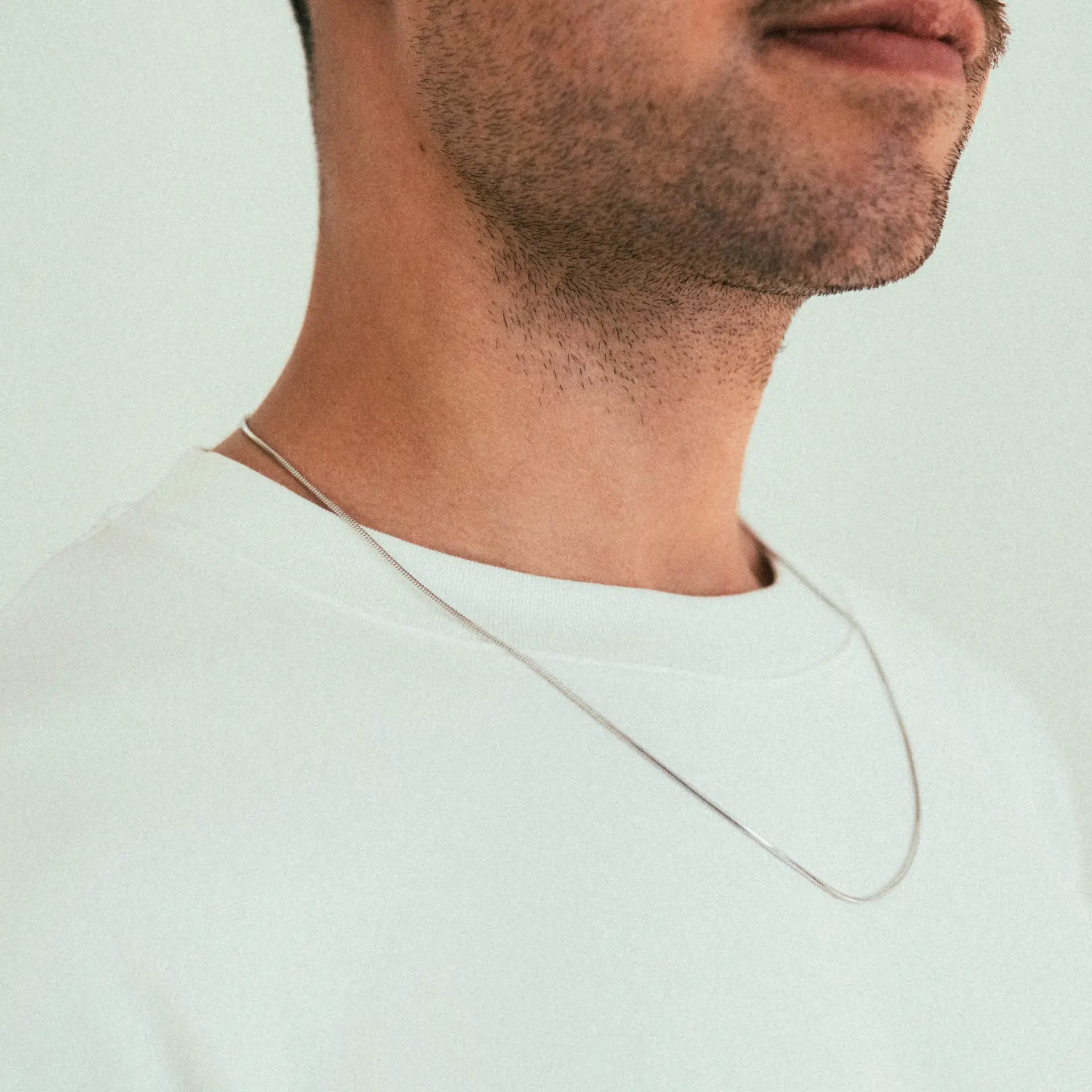 A close-up of a man wearing a white shirt and the WAV Mamba Necklace, featuring his lower face, neck, and jawline against a light background.