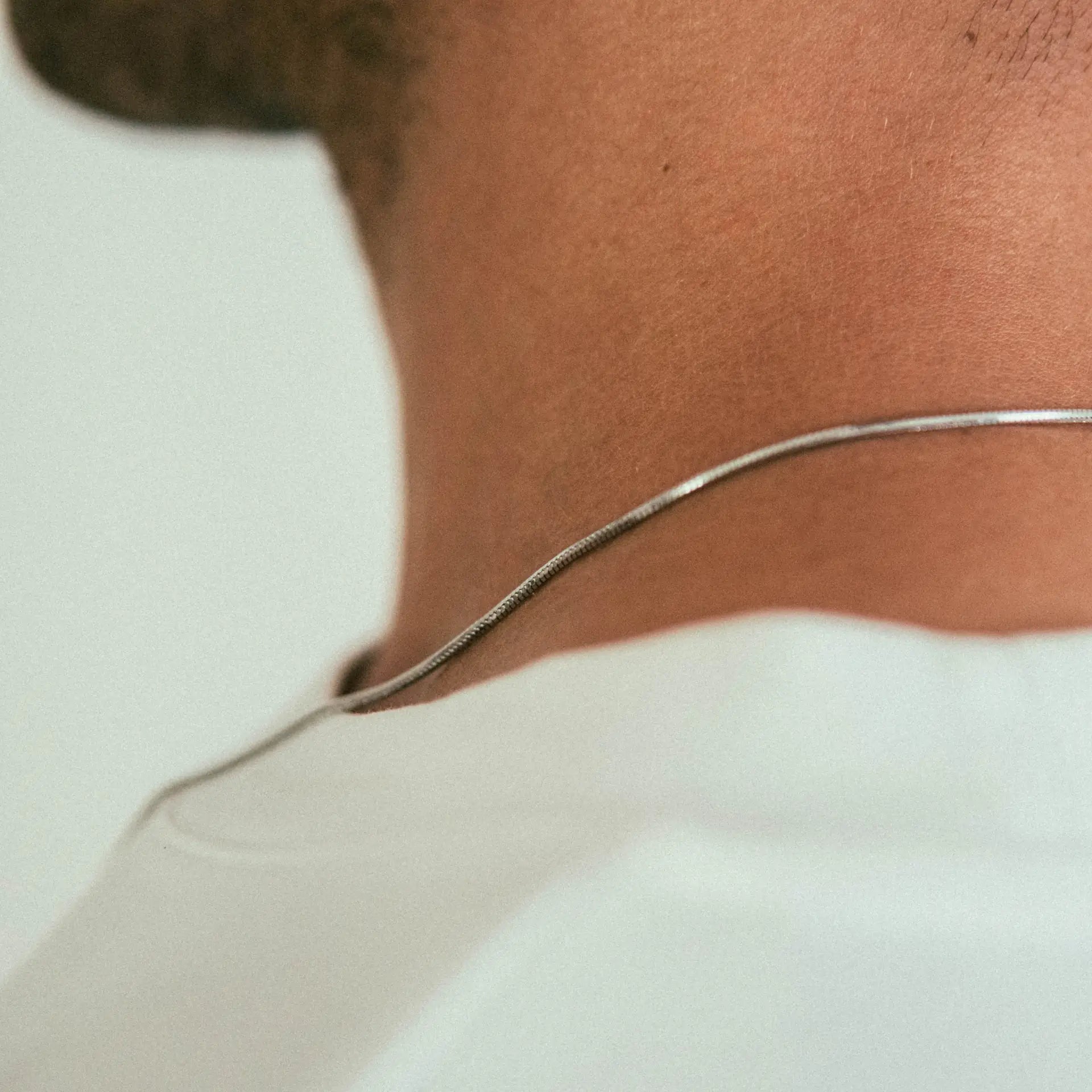 Close-up of the back of a person’s neck wearing the WAV Mamba Necklace with a white shirt. The softly blurred background highlights the neckline and showcases the sleek, minimalist design of this elegant necklace.