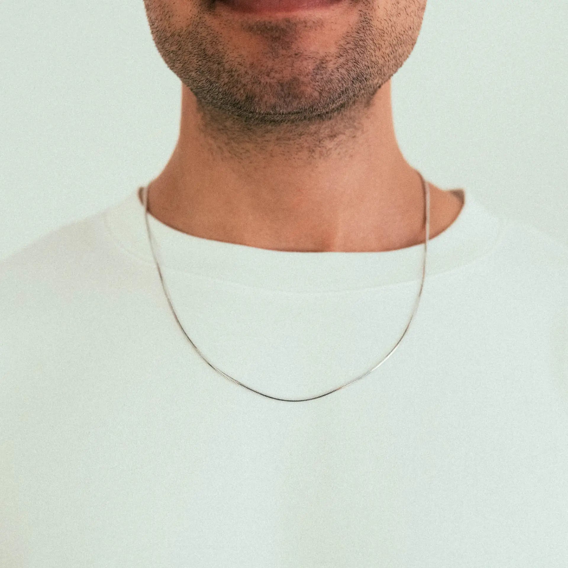 A close-up shows a person in a white shirt wearing the WAV Mamba Necklace. The image highlights their mouth and chin with stubble, set against a plain background.