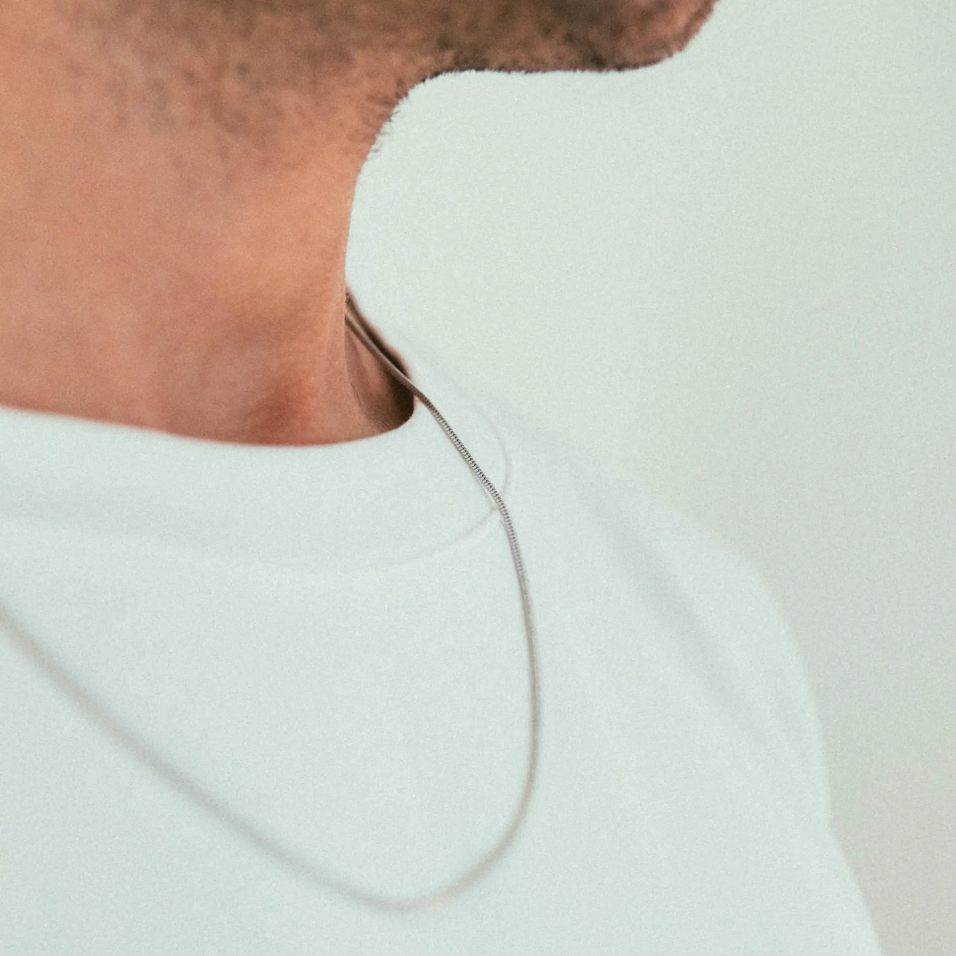 A close-up of a persons neck and lower face shows the WAV Quad Necklace styled with a white t-shirt. A plain, light background highlights the modern design of this minimal jewelry piece.