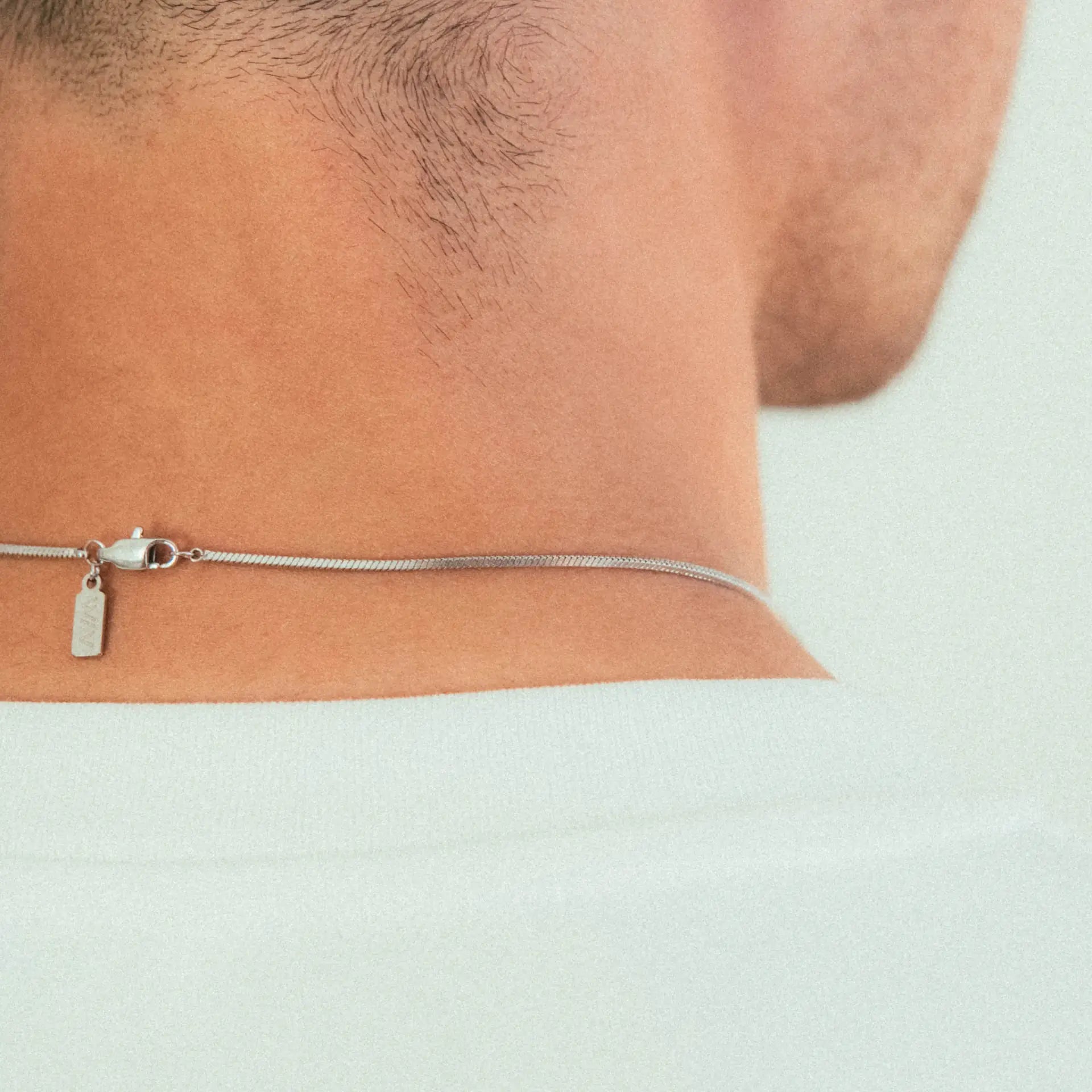 Close-up of a persons neck wearing the WAV Quad Necklace—a modern stainless steel piece with a small rectangular tag and clasp resting above the collar of a white shirt.