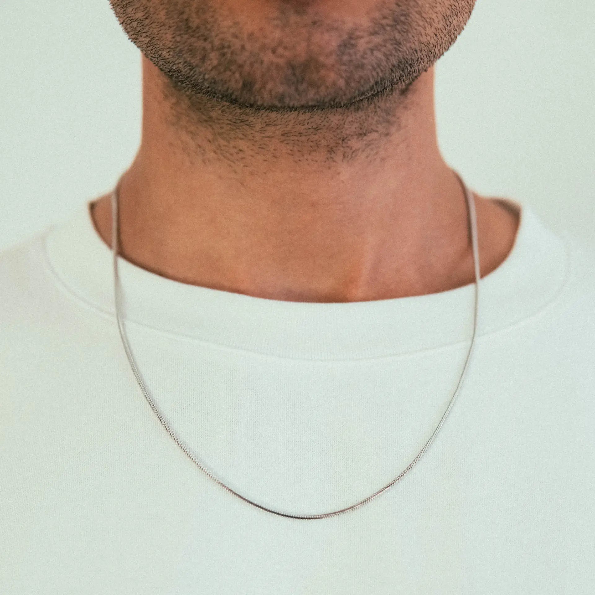 A close-up shows the WAV Quad Necklace worn over a plain white crew-neck shirt. The photo highlights the necklaces modern, minimal design on the neck and upper chest, with no facial features visible.