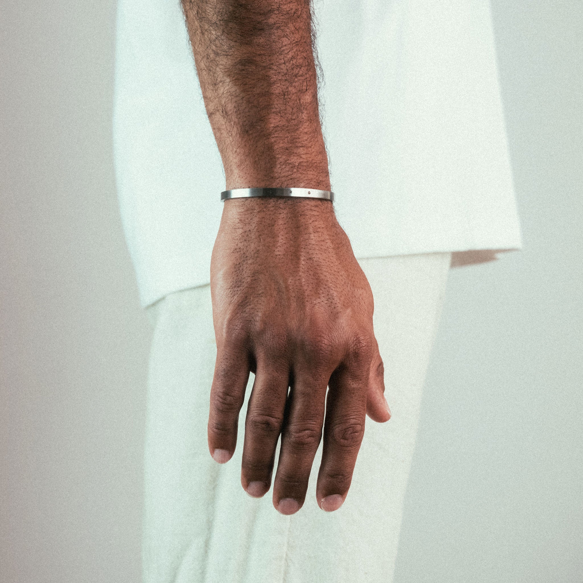Close-up of a person wearing the WAV Custom Cuff Bracelet on their left hand against a neutral background. They are dressed in light-colored clothing, featuring a white top and cream pants.