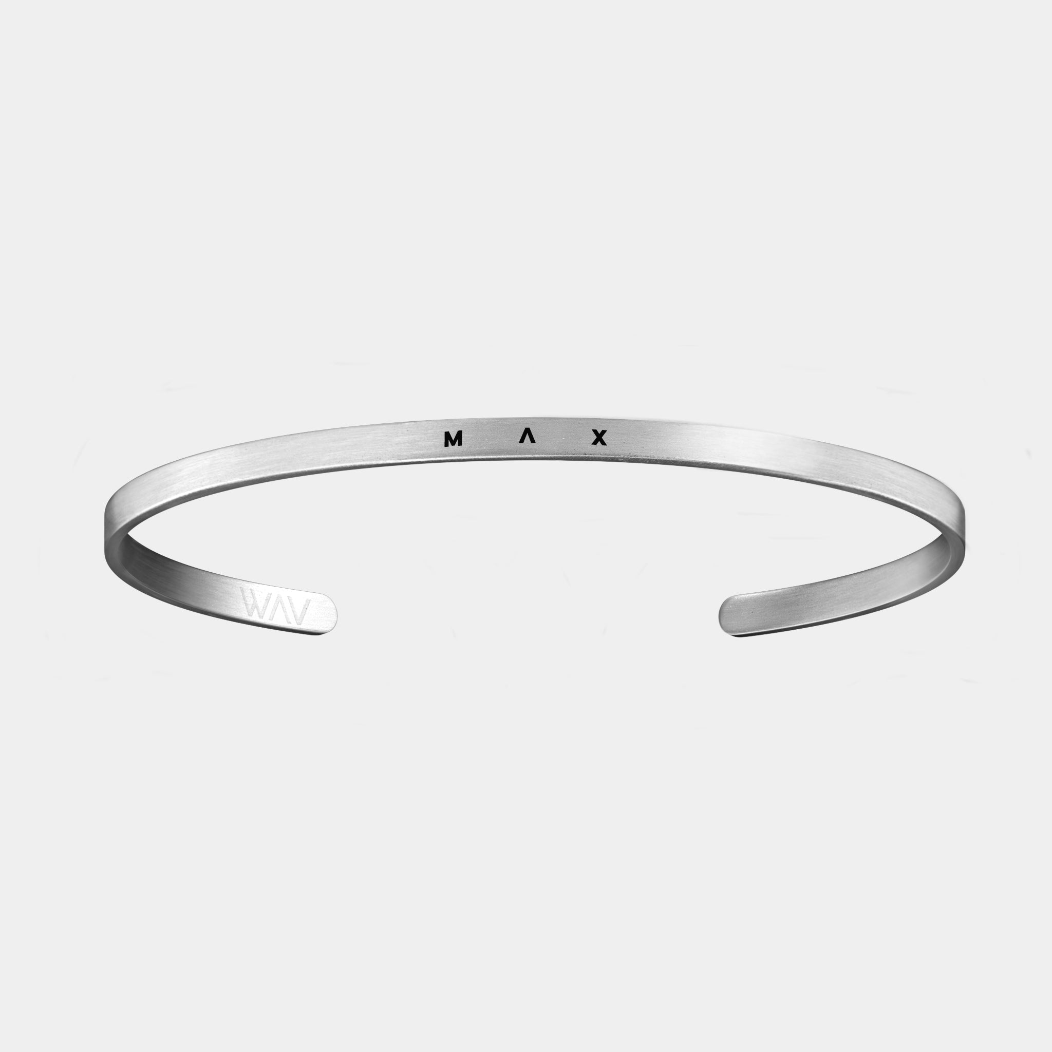 The Custom Cuff Bracelet by WAV is a sleek minimalist silver cuff with a smooth finish and engraved MAX at the center. Open-ended for a modern design, it offers unique style on a light gray background, ideal for those seeking custom jewelry to enhance their look.