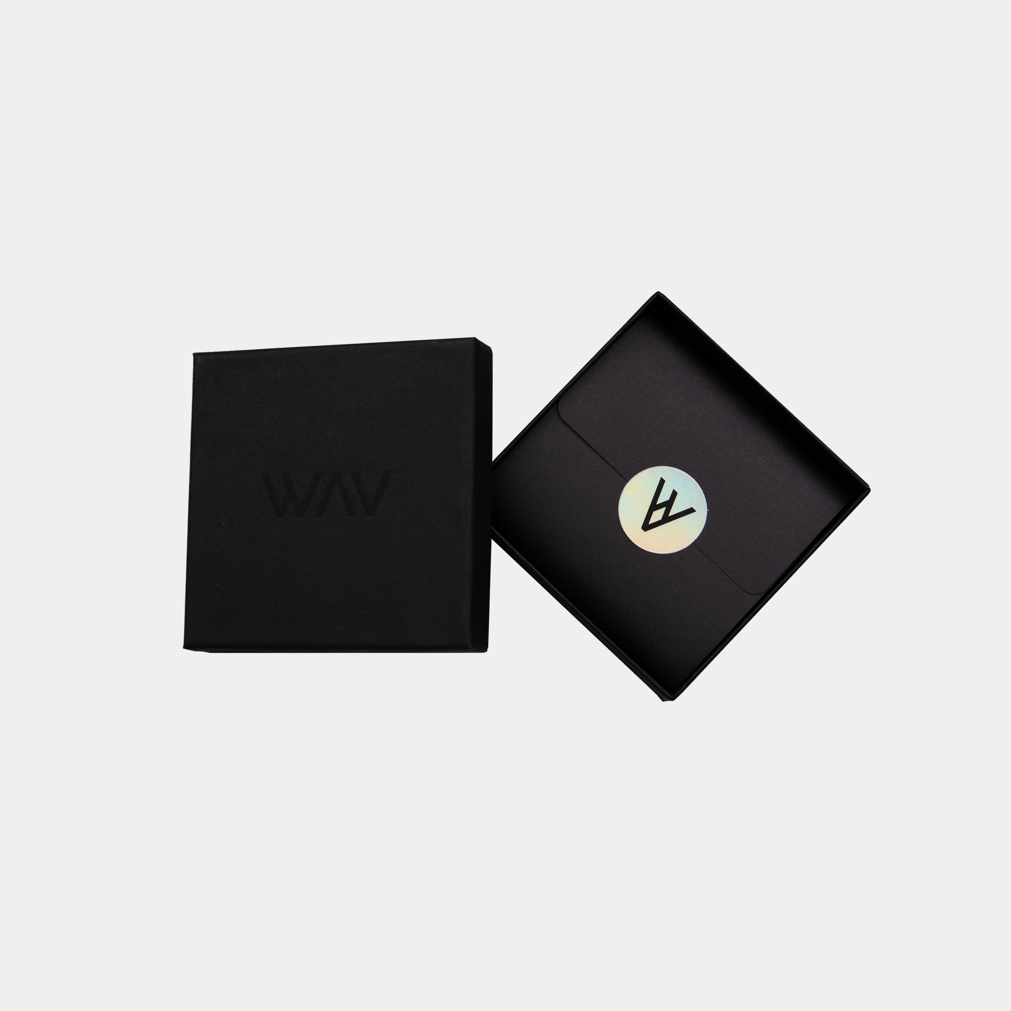 A black, square Premium gift box from WAV partially opens to reveal a folder with a round metallic logo sticker. The lid features a subtle embossed WAV text, enhancing the allure of custom jewelry inside against a plain white background.