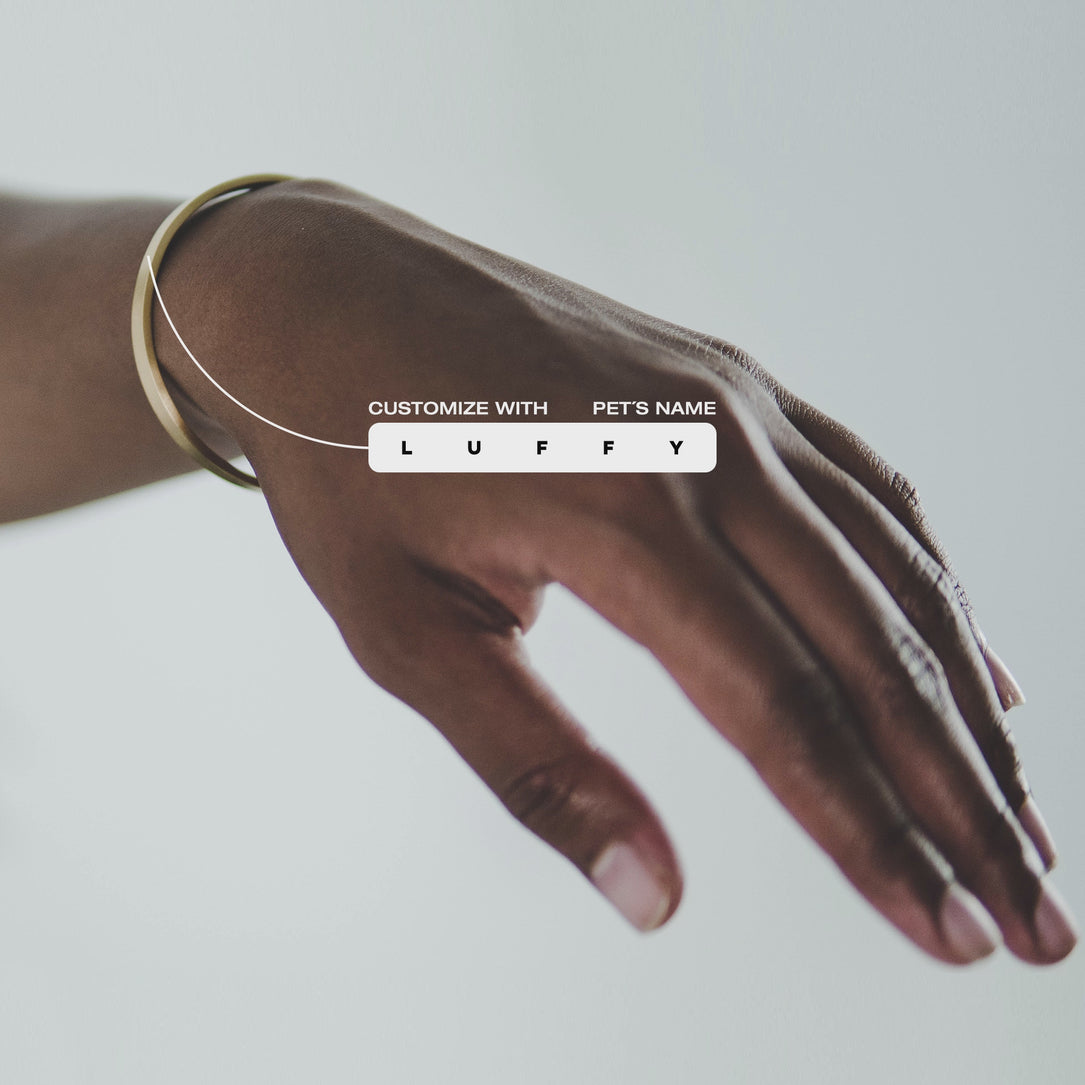 Custom cuff bracelet on a woman's wrist, made of stainless steel with 18k gold PVD plating, customized and personalized with Morse code, coordinates, names, initials, dates, or custom text. Minimalist unisex jewelry, displayed against a blue background